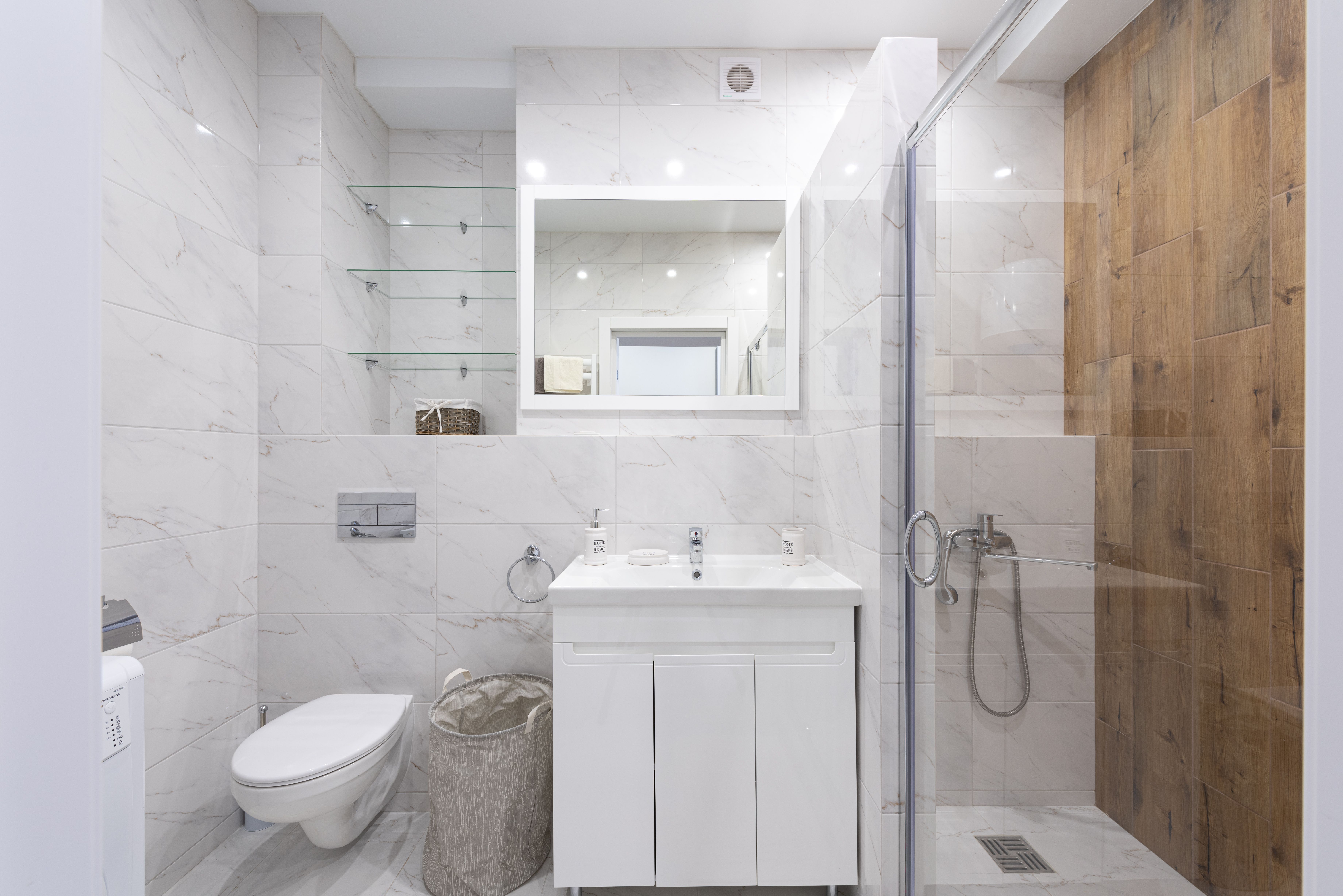 Baño moderno reformado con azulejo de mármol y mampara de ducha de cristal.